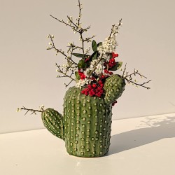Vase cactus vert garni de fleurs séchées posé sur un meuble blanc, à la lumière rasante.