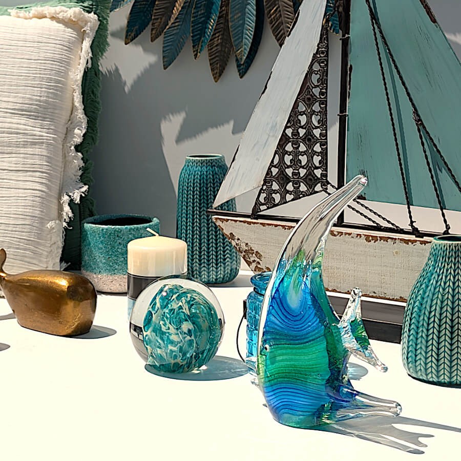 Poisson en verre soufflé exposé devant un bateau décoratif et des vases turquoises.