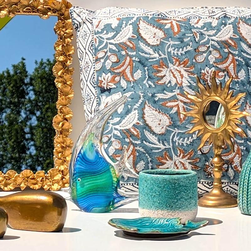 Poisson sculptural en verre bleu posé près d'un miroir doré et d'un coussin aux motifs marins.