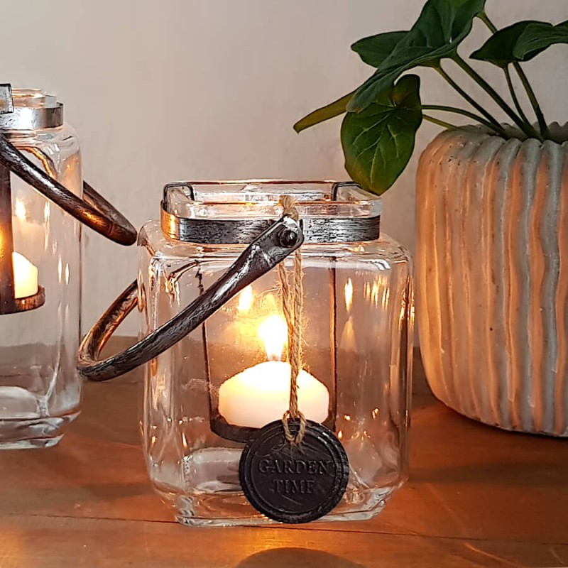 Photophore carré allumé avec bougie chauffe-plat posé sur un meuble en bois chaleureux.