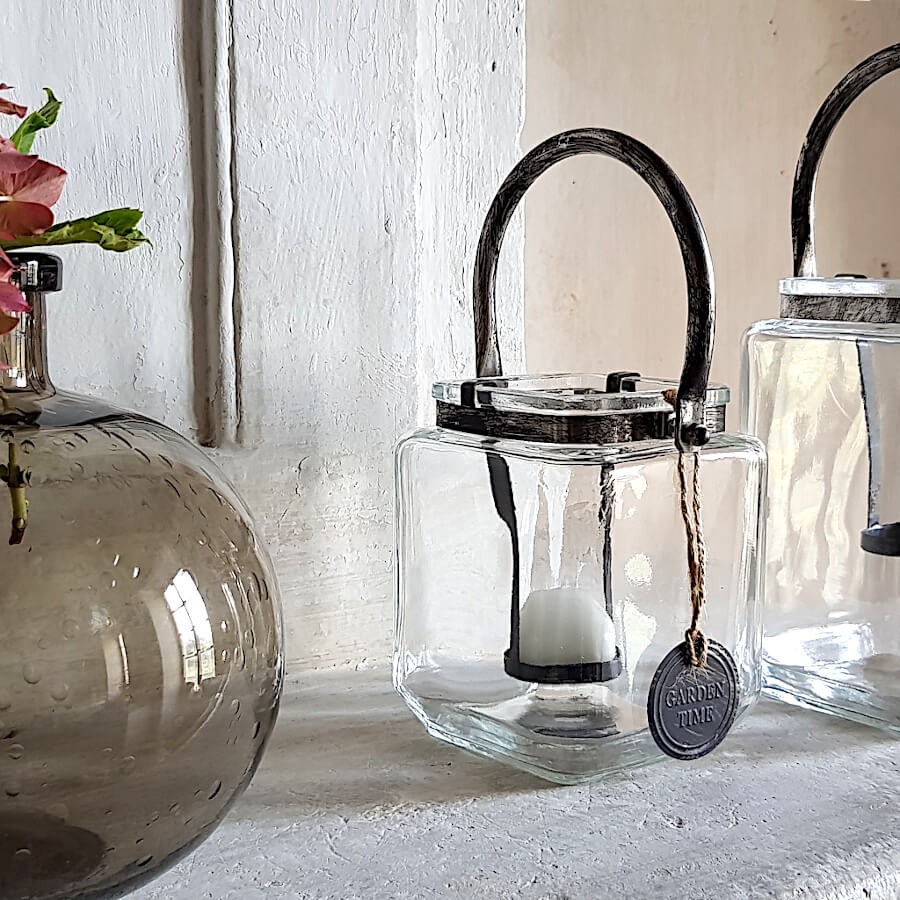 Photophore rétro en verre et métal sur une cheminée en pierre avec fleurs séchées.
