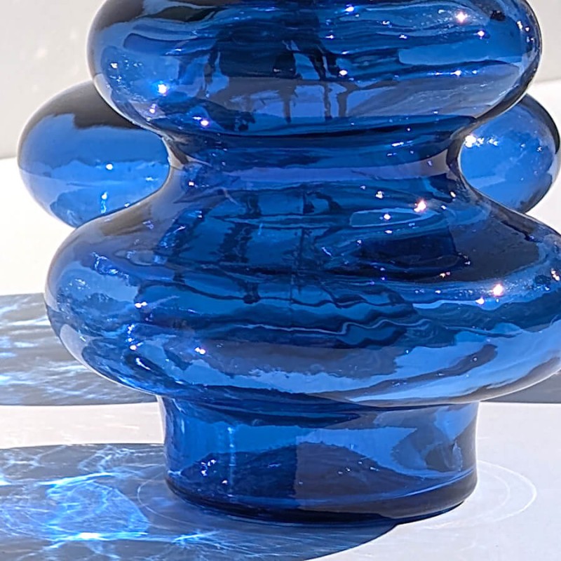 Gros plan sur les courbes bulbeuses et l'ombre bleutée projetée du vase en verre.