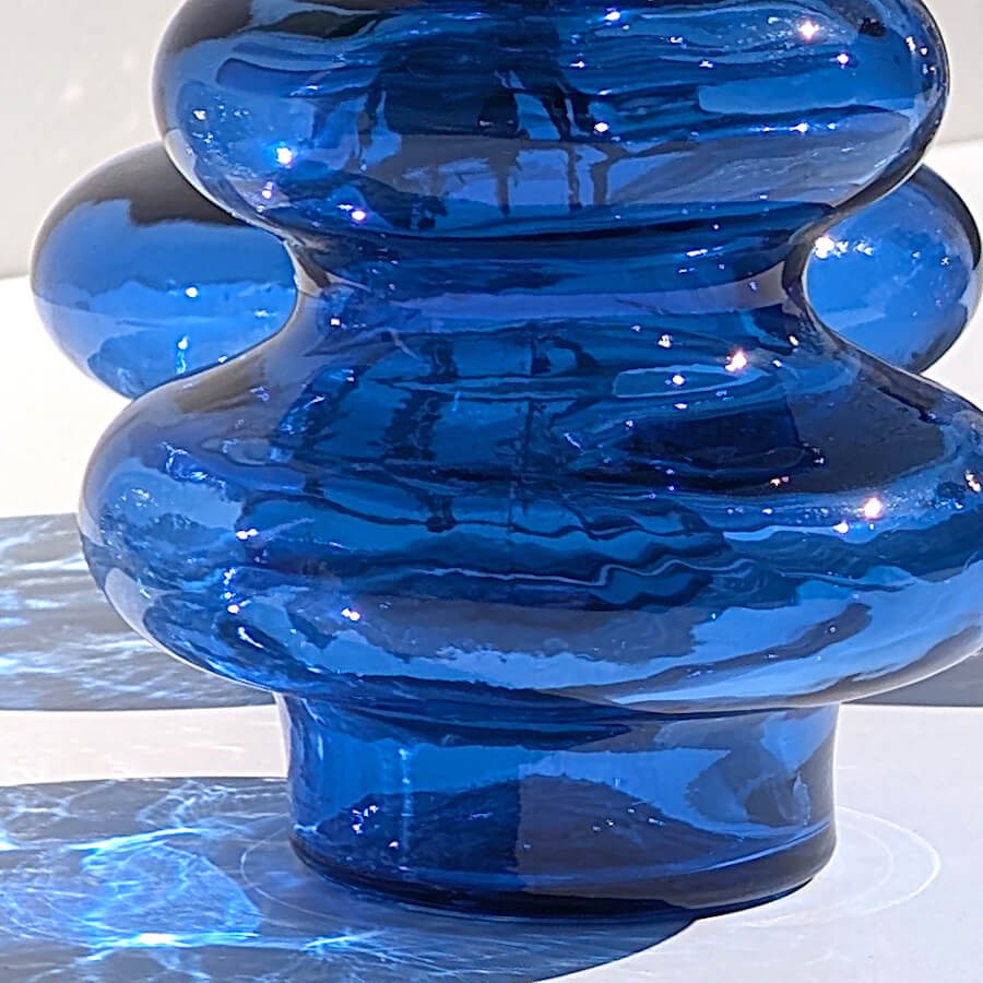 Gros plan sur les courbes bulbeuses et l'ombre bleutée projetée du vase en verre.