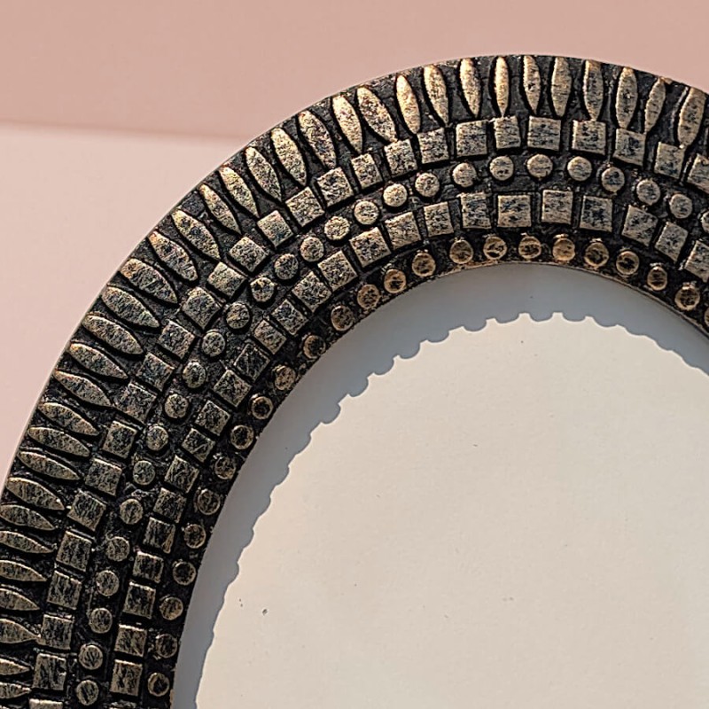 Gros plan sur les motifs géométriques sculptés en écailles et la patine bronze de la résine.