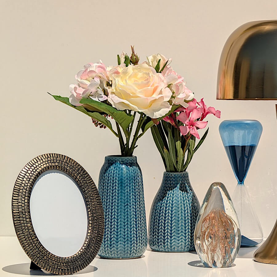 Cadre photo ovale exposé au milieu de vases bleus et d'une lampe dorée Deco Delight sur un buffet.