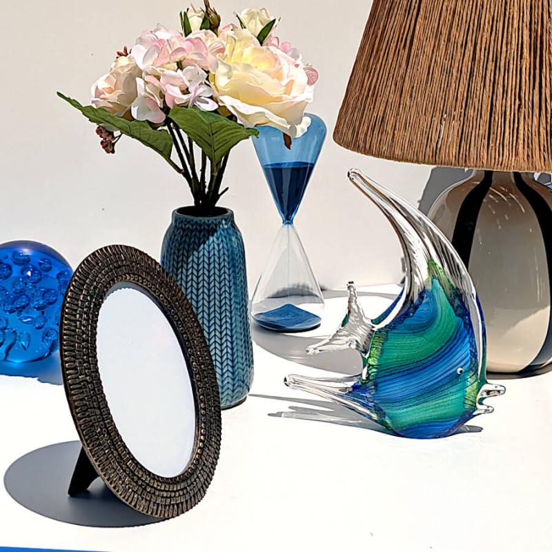 Cadre photo ovale en résine bronze près du poisson en verre soufflé et de la lampe en raphia de la collection Deco Delight.