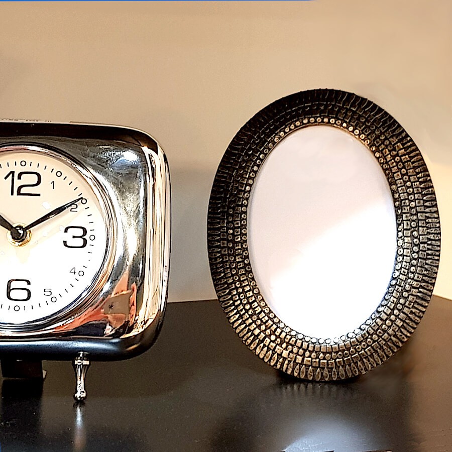 Cadre photo ovale posé à côté d'une horloge rétro argentée sur un meuble.