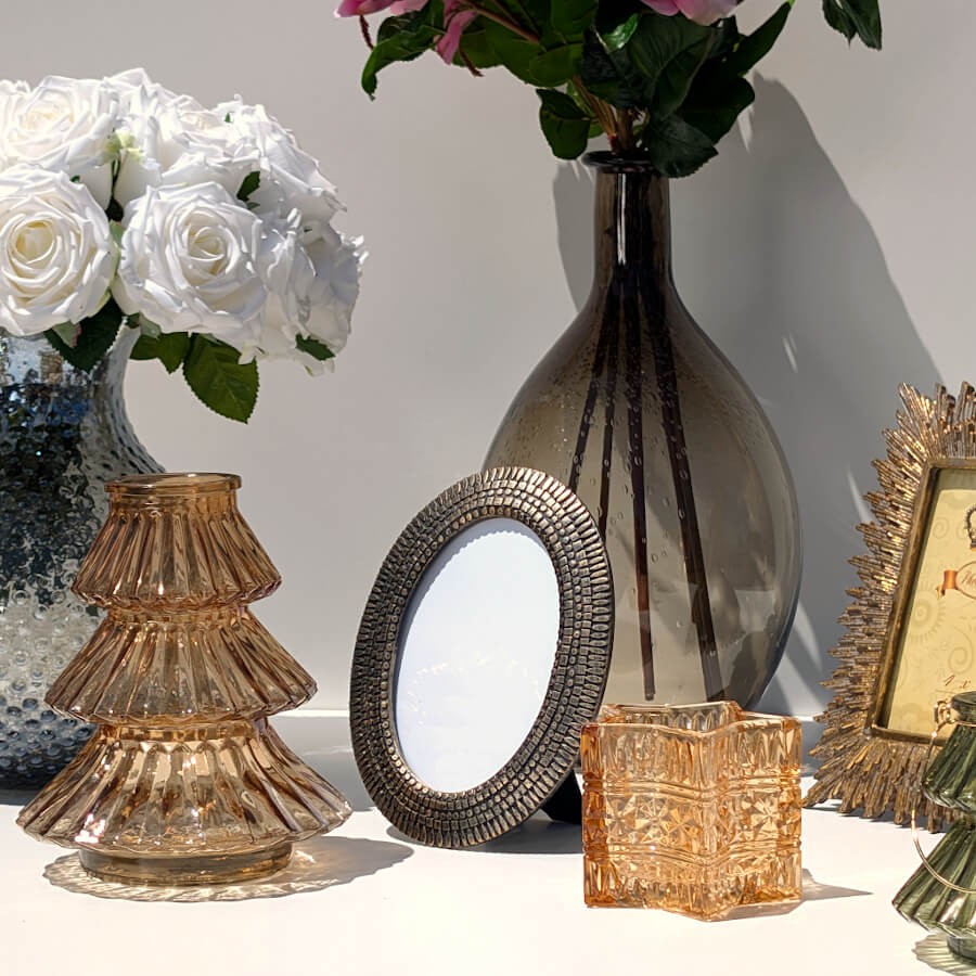 Composition déco chic comprenant le cadre photo ovale bronze, un vase en verre et un photophore.
