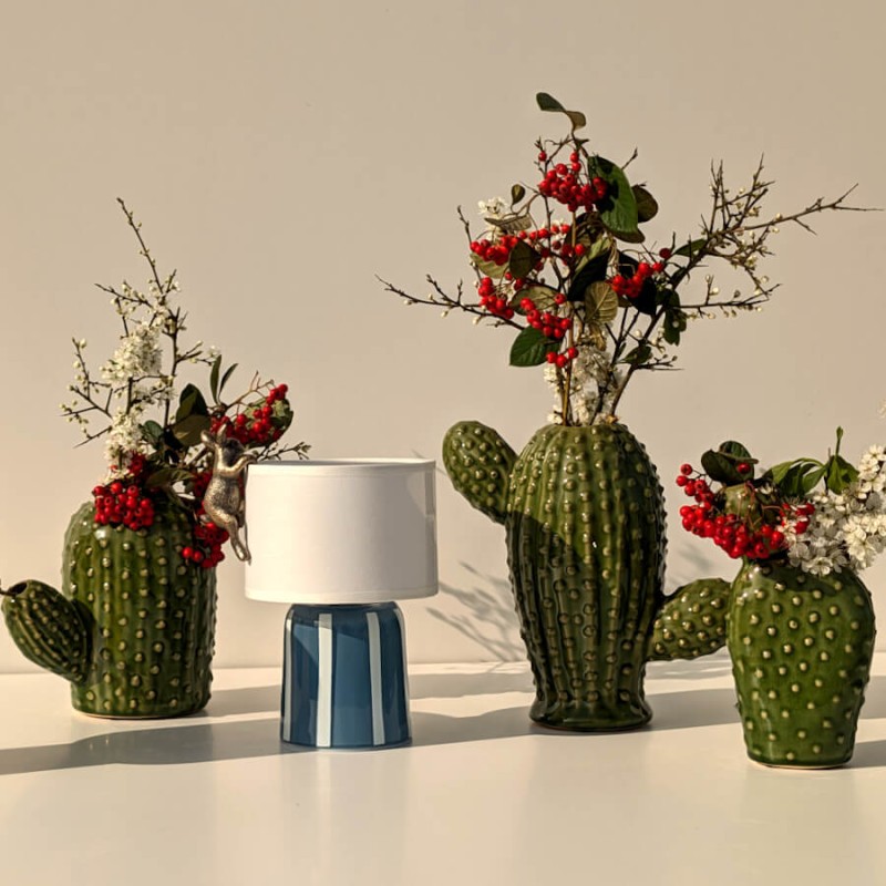 Trio de vases cactus en céramique garnis de fleurs rouges et blanches près d'une lampe LED nomade bleue.
