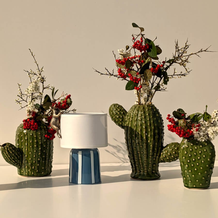 Trio de vases cactus en céramique garnis de fleurs rouges et blanches près d'une lampe LED nomade bleue.