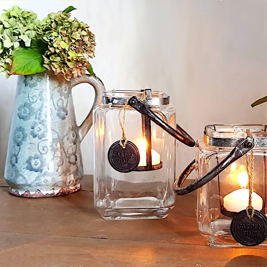 Ambiance chaleureuse avec lanternes carrées en verre allumées et pichet décoratif sur table en bois rustique.