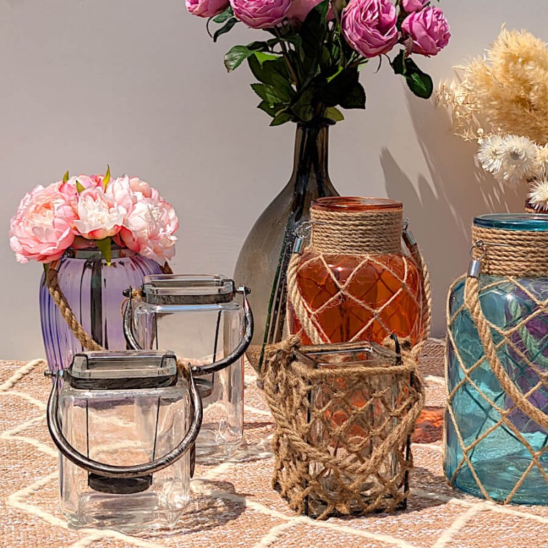 Composition de lanternes en verre et cordage coloré sur nappe rosée.