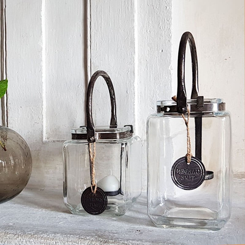 Les deux formats de lanternes carrées en verre et métal patiné présentés ensemble sur cheminée pierre.