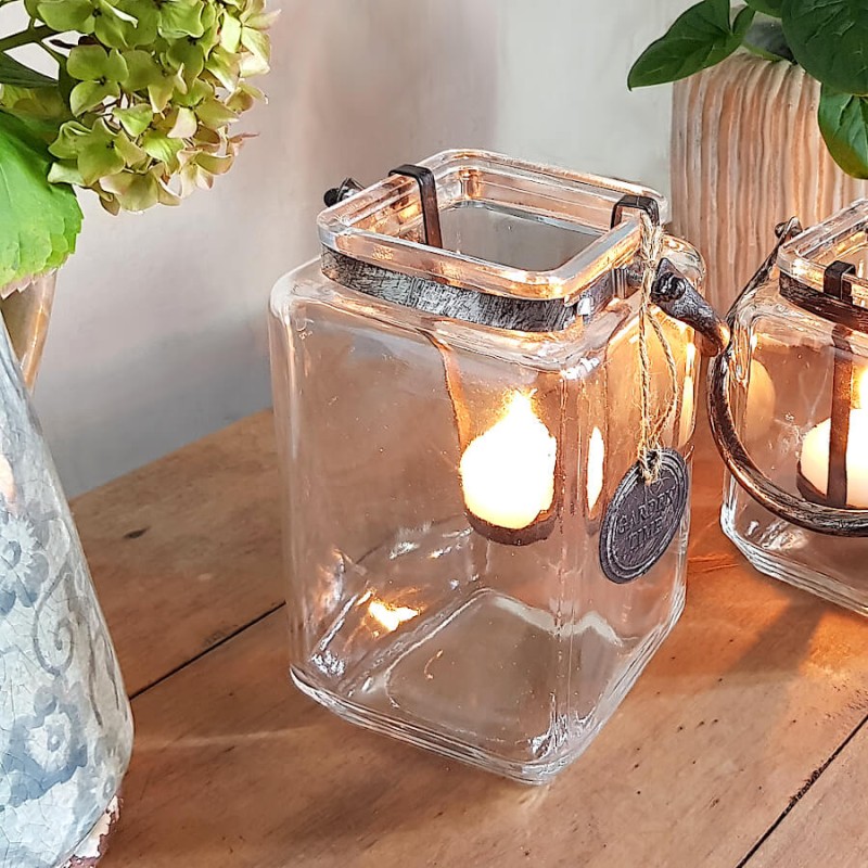 Lanterne carrée grand modèle H18 cm allumée avec une bougie chauffe-plat dans un décor chaleureux.