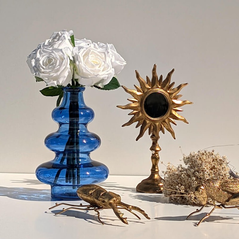 Composition lumineuse avec vase bleu 3 boules, roses blanches, miroir soleil et sauterelle dorée.