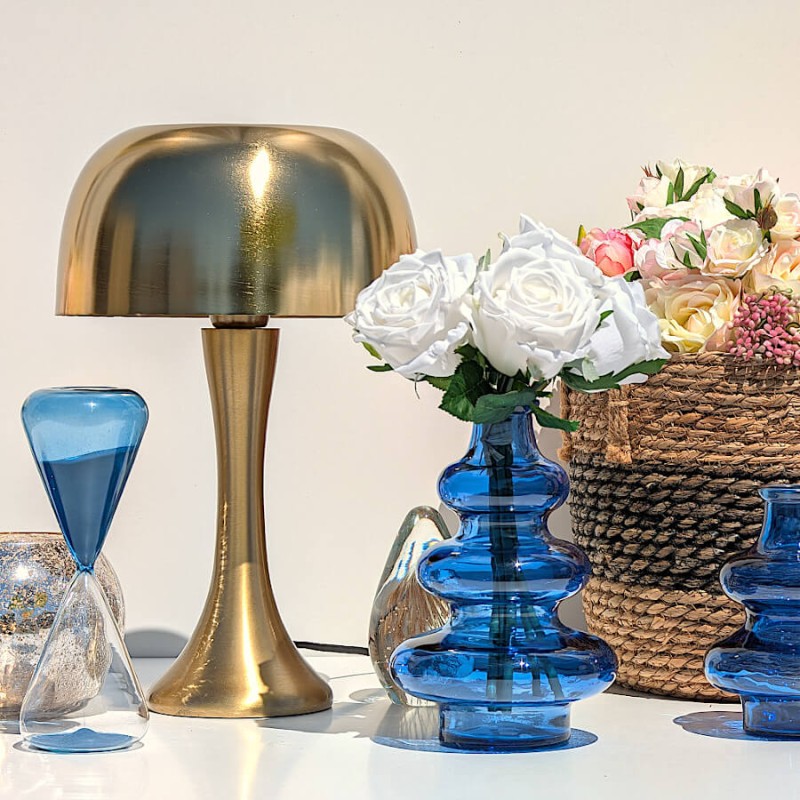 Vase 3 boules bleu cobalt garni de roses blanches à côté d'une lampe dorée et d'un sablier bleu.