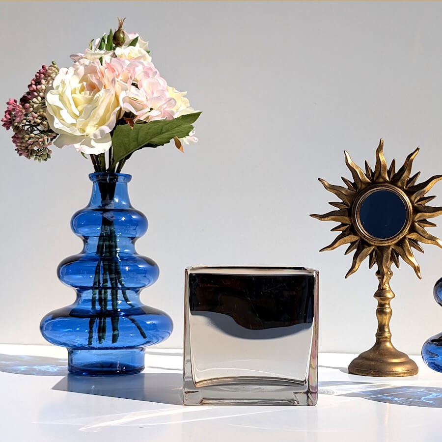 Composition déco avec vase en verre bleu 3 boules fleuri, photophore carré et miroir soleil doré.
