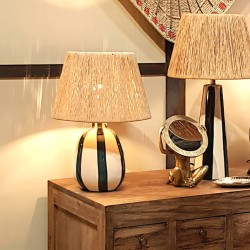 Lampe à poser Riviera allumée posée sur une enfilade en bois massif avec objets déco.