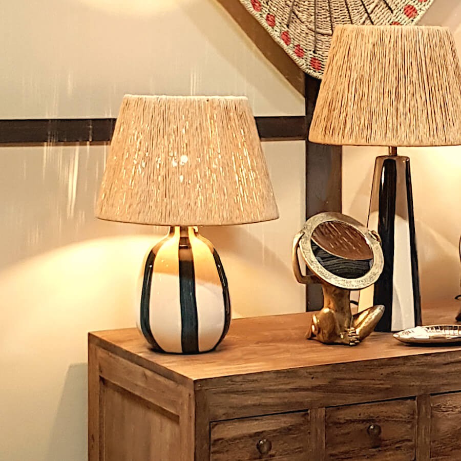 Lampe à poser Riviera allumée posée sur une enfilade en bois massif avec objets déco.