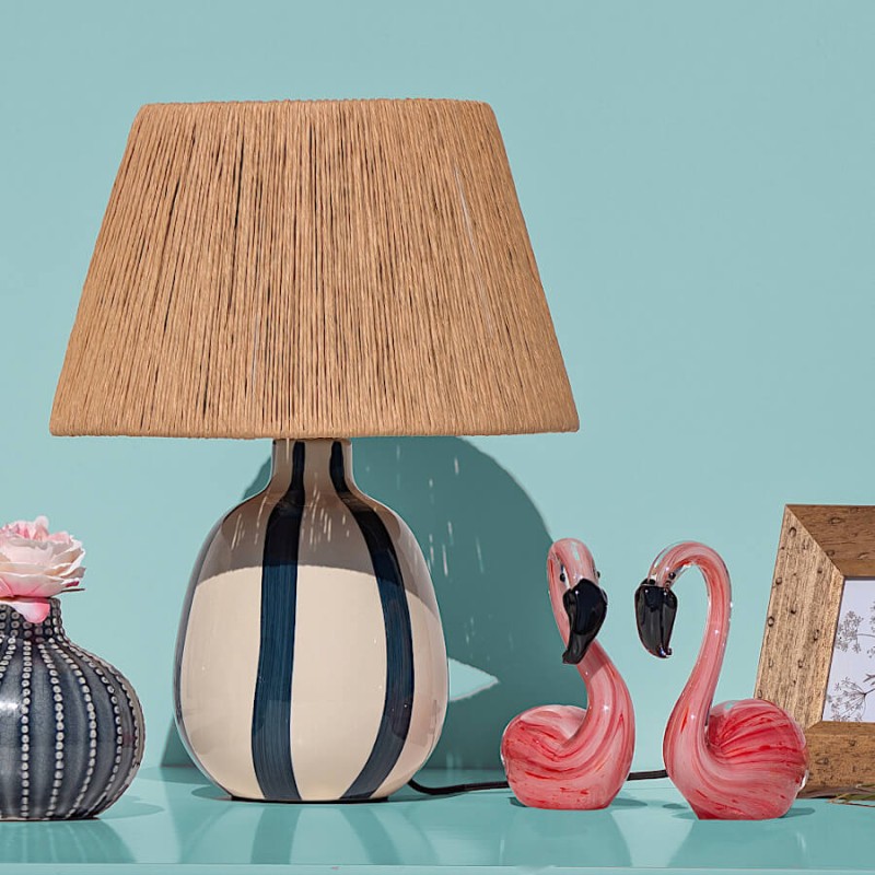 Lampe Riviera présentée sur fond bleu à côté de figurines flamants roses.