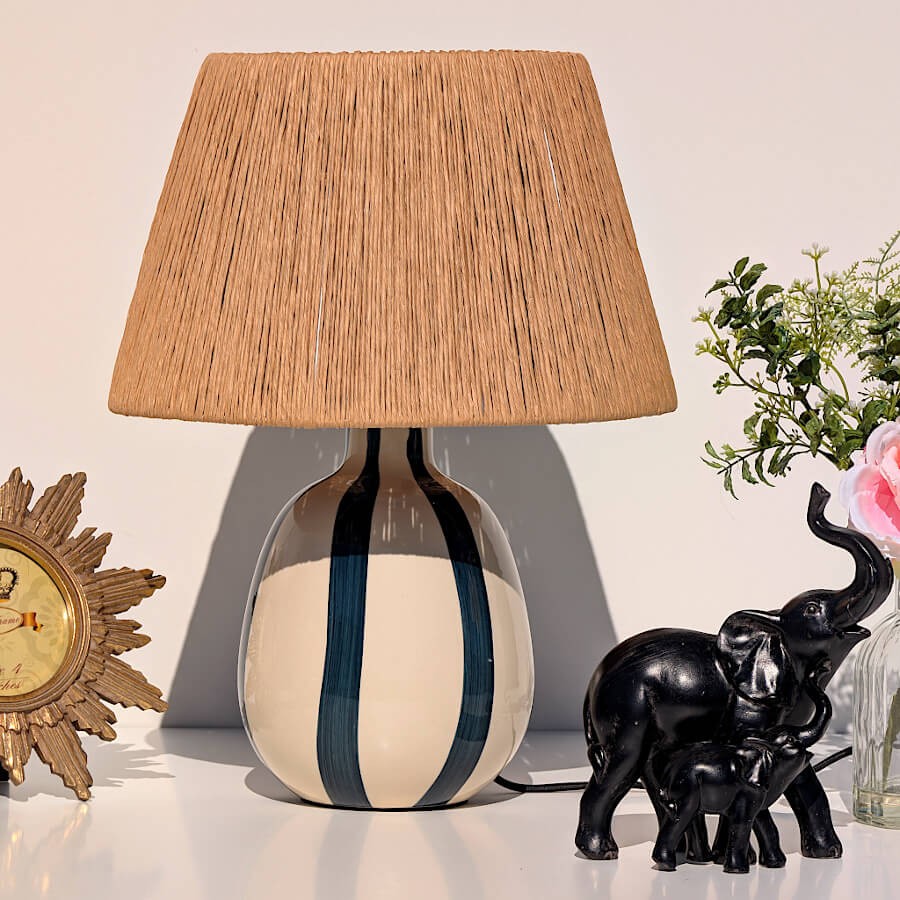 Lampe Riviera posée sur meuble blanc avec éléphant noir et miroir soleil.