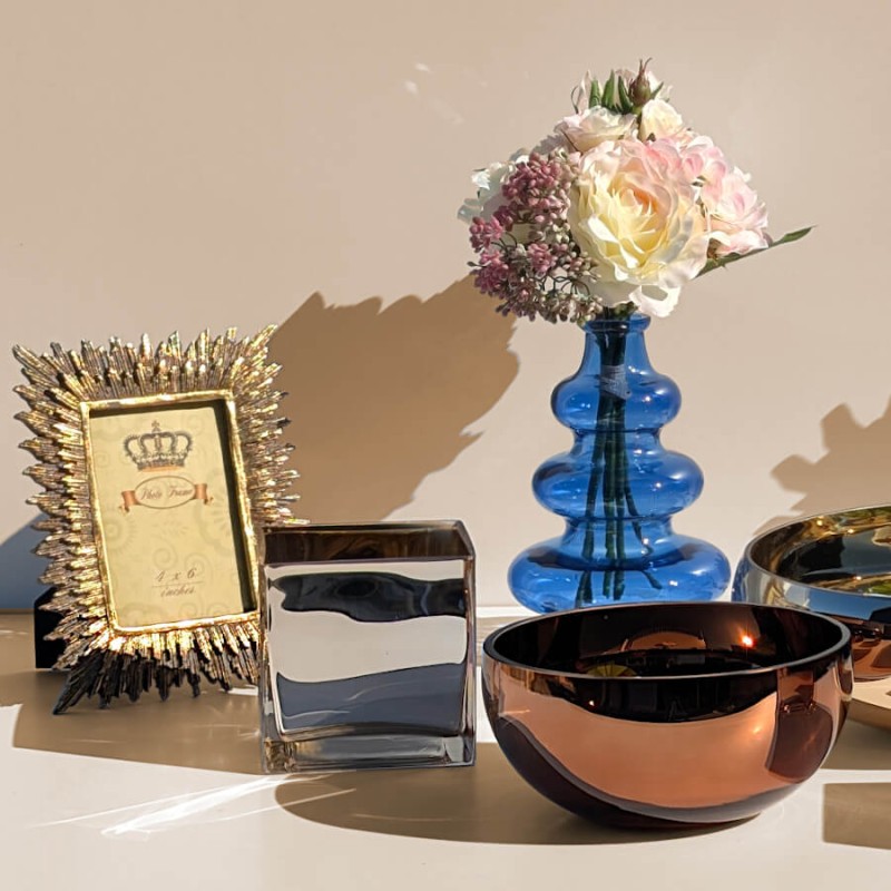 Cadre photo baroque doré présenté dans un ensemble déco avec vase bleu et photophore carré.
