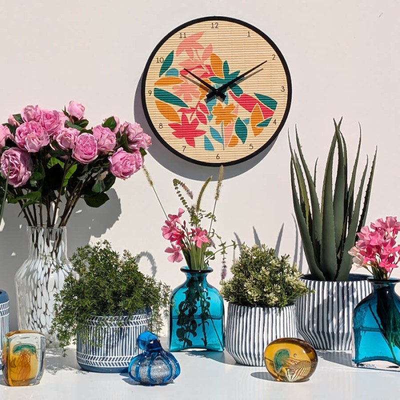 Ensemble décoratif mural avec horloge bambou tropicale, bouquet de roses roses, vases bleus et cache-pots cannelés.