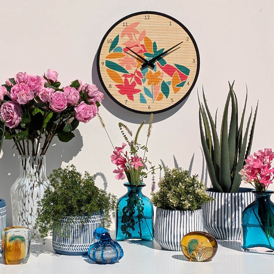 Ensemble décoratif mural avec horloge bambou tropicale, bouquet de roses roses, vases bleus et cache-pots cannelés.