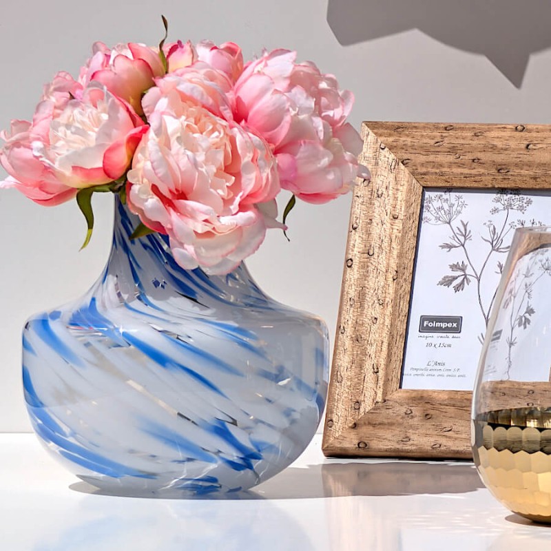 Vase marbré bleu garni de pivoines roses à côté d'un cadre photo aspect bois.