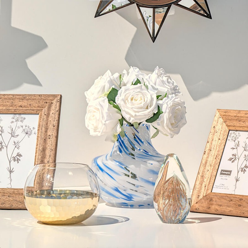 Composition florale avec roses blanches dans le vase marbré bleu, entouré d'accessoires dorés.