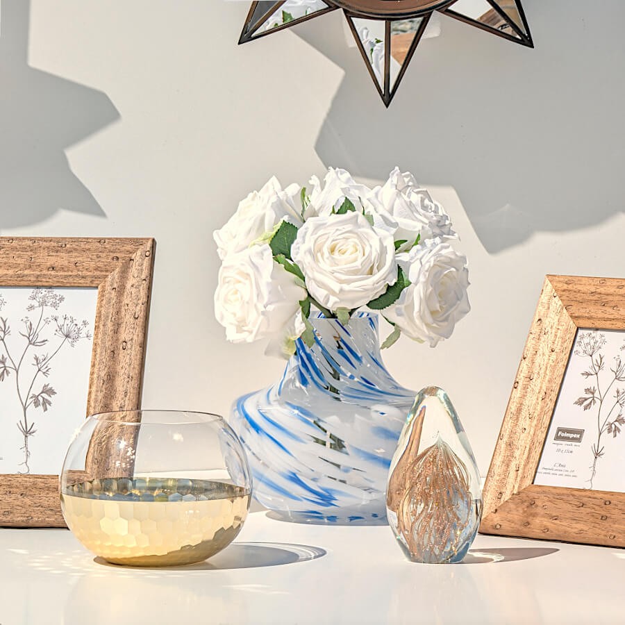 Composition florale avec roses blanches dans le vase marbré bleu, entouré d'accessoires dorés.