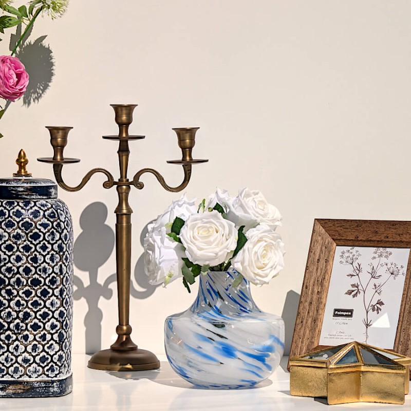 Décoration avec vase émaillé motif ethnique bleu, candélabre classique et vase opalin bleu garni de roses blanches.
