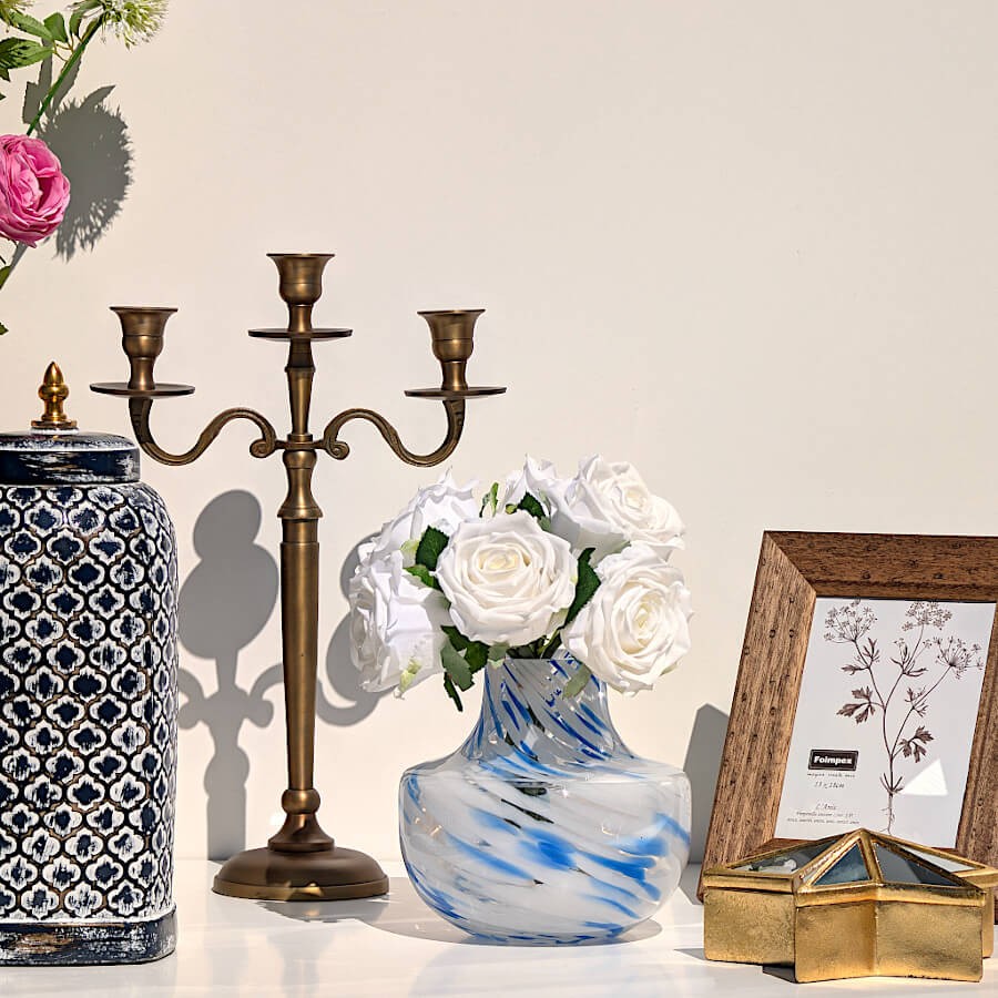 Décoration avec vase émaillé motif ethnique bleu, candélabre classique et vase opalin bleu garni de roses blanches.