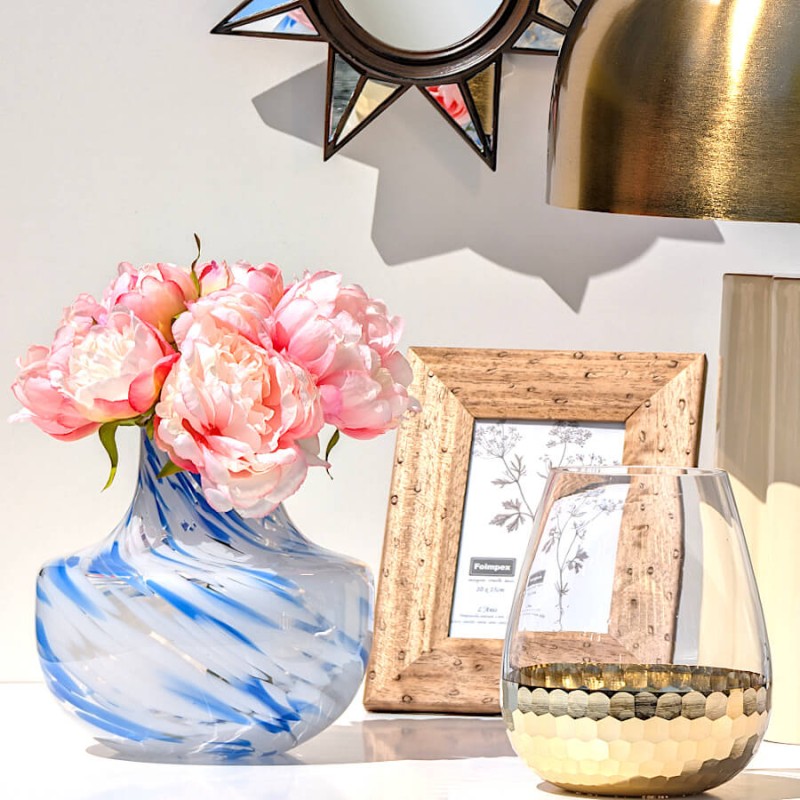 Composition élégante avec pivoines roses dans le vase opalin bleu et miroir soleil doré en arrière-plan.