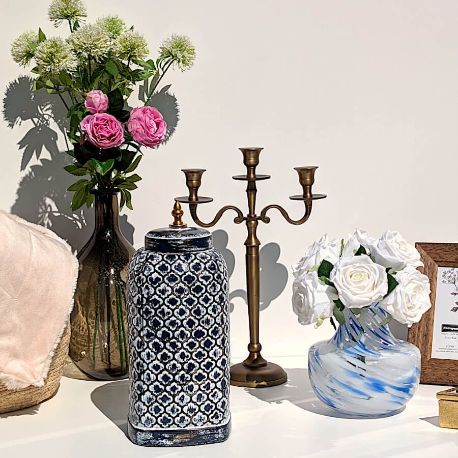 Scène déco associant le vase opalin bleu garni de roses blanches, un vase en céramique ethnique et un candélabre.