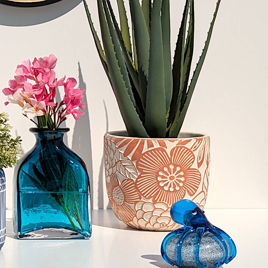 Cache-pot en ciment terracotta garni d'une plante verte posé à côté d'un vase en verre bleu et d'une pieuvre déco en verre.