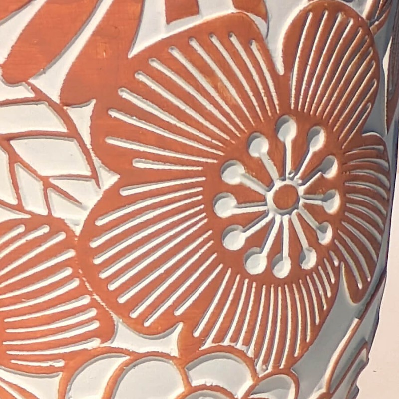 Gros plan sur les motifs de fleurs seventies gravés en relief blanc sur la céramique ciment terracotta.