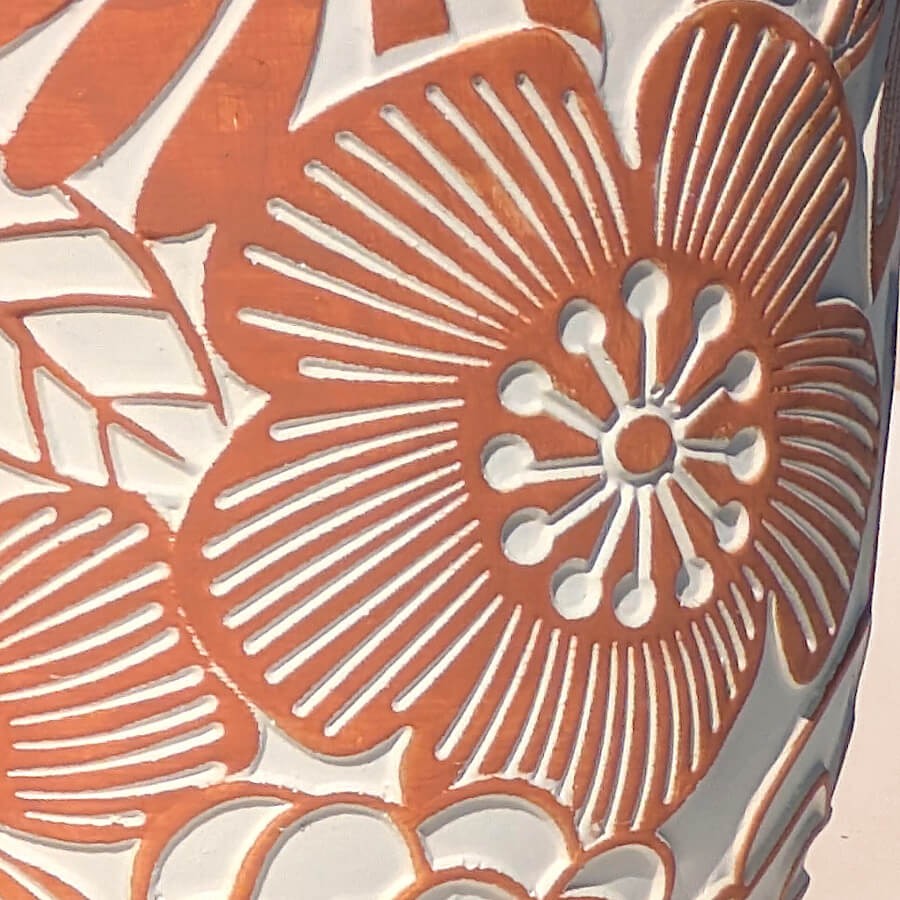 Gros plan sur les motifs de fleurs seventies gravés en relief blanc sur la céramique ciment terracotta.