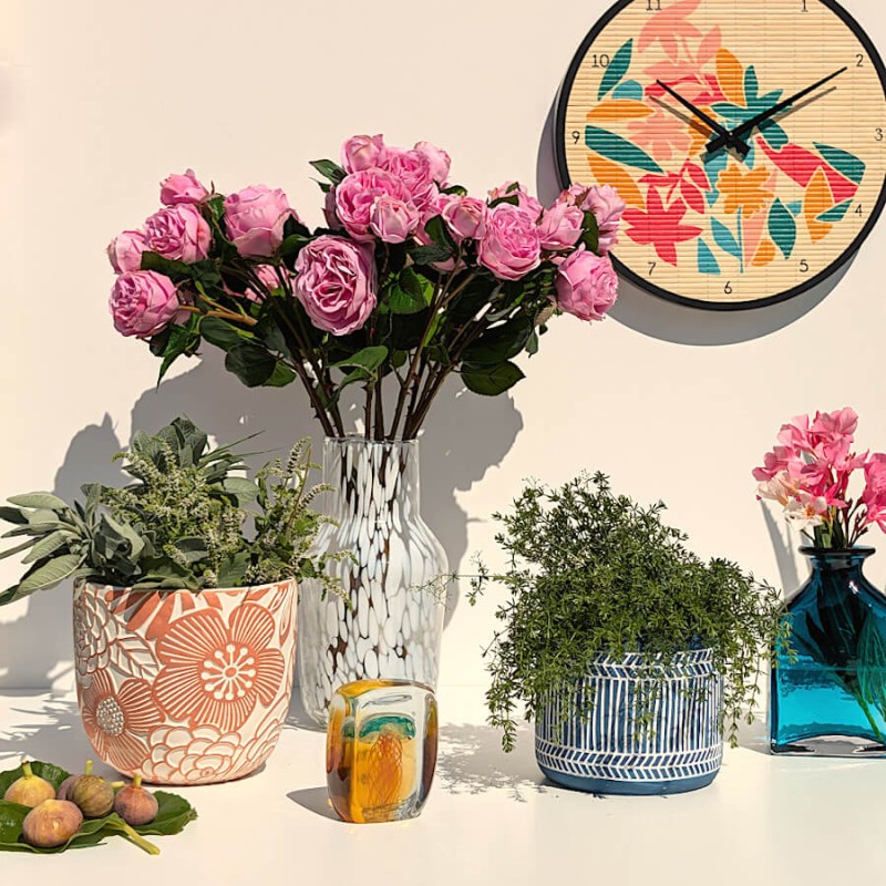 Ambiance bucolique avec le cache-pot terracotta, un bouquet de roses roses et divers objets décoratifs.