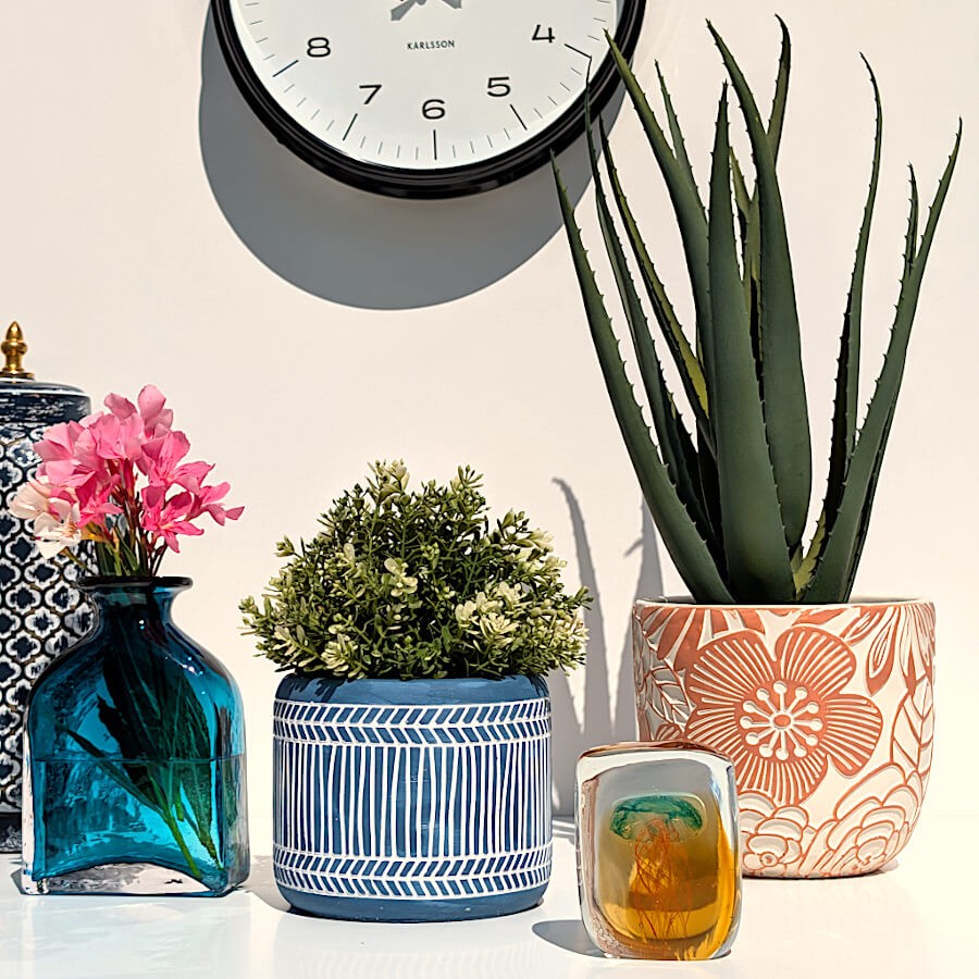 Décoration de buffet ensoleillée avec cache-pot terracotta, vase bleu nuit et horloge murale.