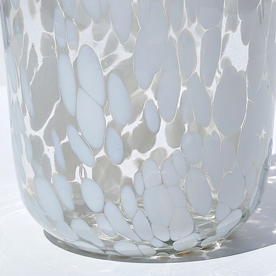 Gros plan sur la texture du verre transparent et les confettis blancs incrustés dans la matière.