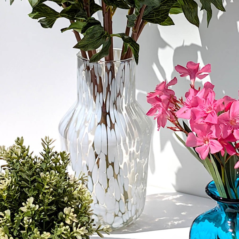 Composition florale avec pivoines roses dans le vase à confettis à côté d'un flacon en verre bleu.