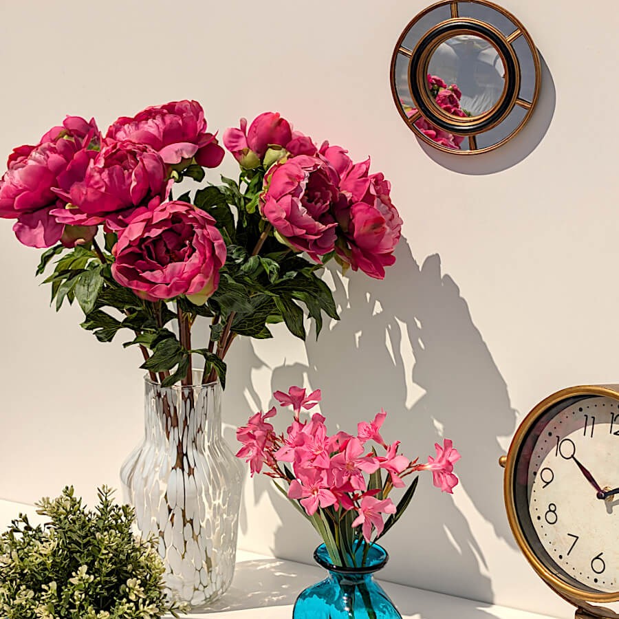 Magnifique composition de pivoines fuchsia artificielles dans le vase en verre recyclé transparent à tâches blanches.