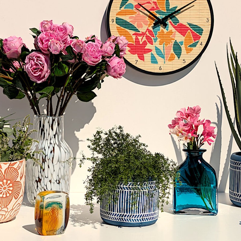 Décoration murale complète avec le vase fleuri, l'horloge bambou tropicale et des plantes vertes.
