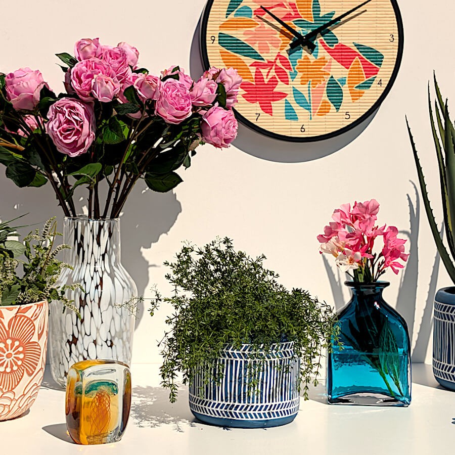 Décoration murale complète avec le vase fleuri, l'horloge bambou tropicale et des plantes vertes.