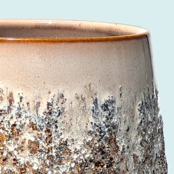 Gros plan sur l'émail brut moucheté et la texture rugueuse du cache-pot beige et brun.