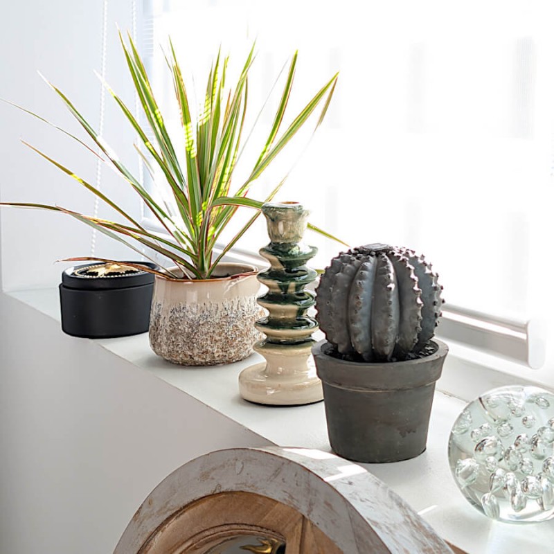 Cache-pot en céramique texturée posé sur un rebord de fenêtre avec une statuette cactus en ciment.