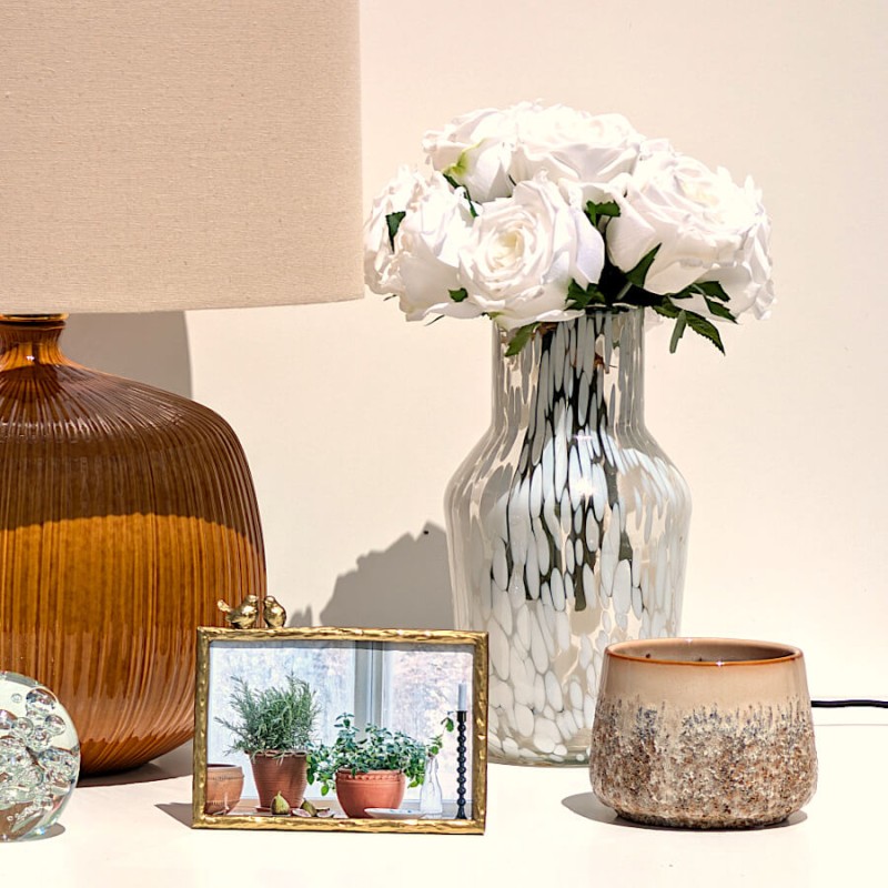 Composition de buffet avec lampe en grès ocre, vase fleuri et petit cache-pot beige.