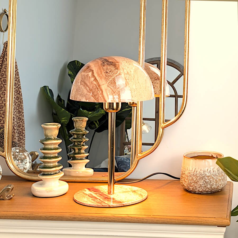 Ambiance chic sur console avec miroir Art Déco, lampe en onyx brun, chandelier vert et cache-pot.