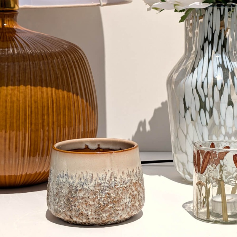 Petit cache-pot texturé beige posé à côté d'une grande lampe en grès strié ambré.